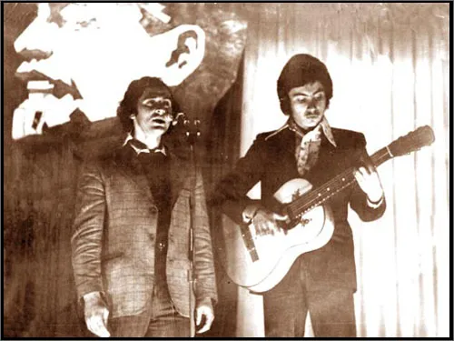 Jan playing acoustic guitar beside a singer in 1974