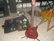 A red Brian Moore MIDI guitar on a stand next to a pedalboard